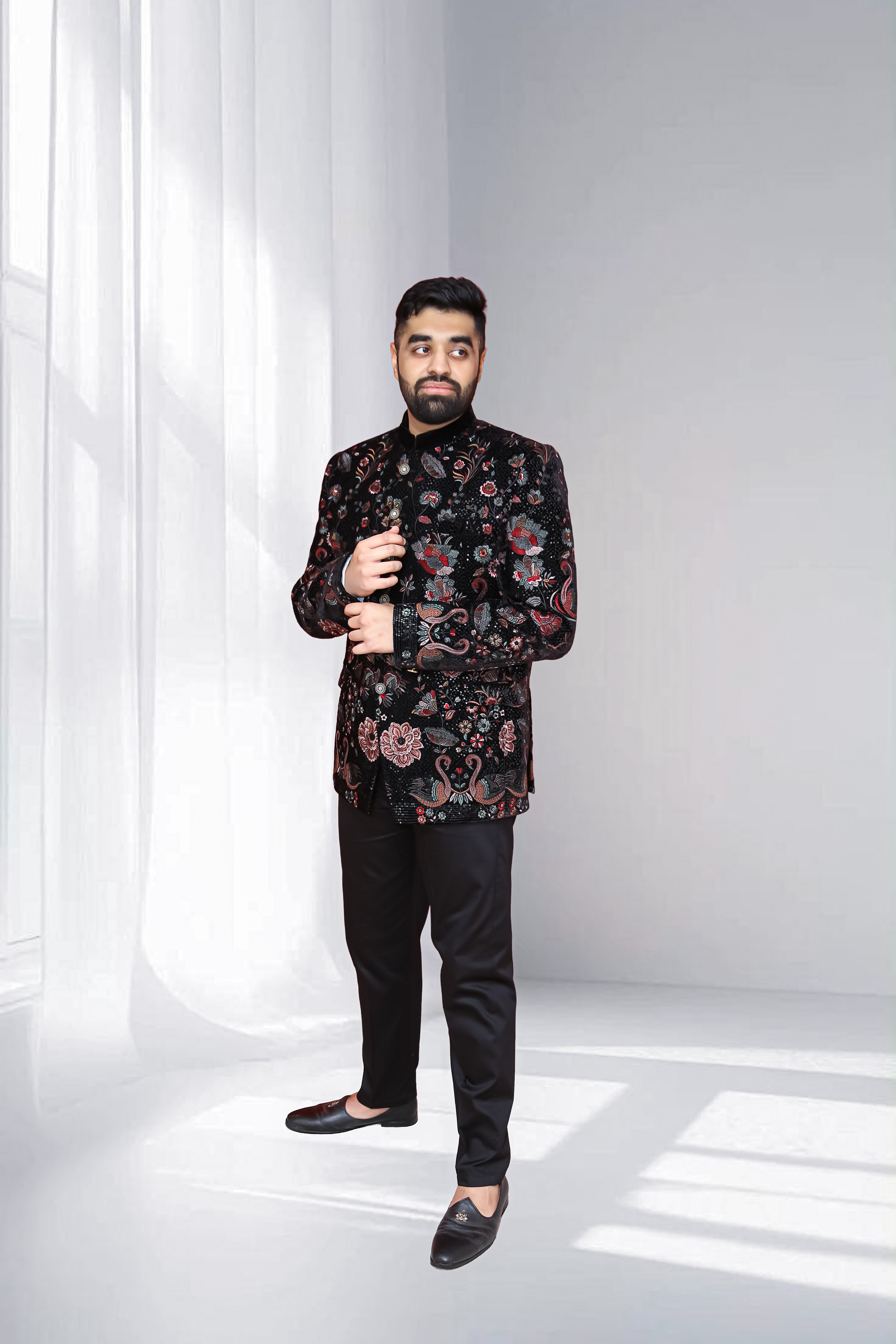 Man wearing a black floral patterned shirt and black pants against a white background