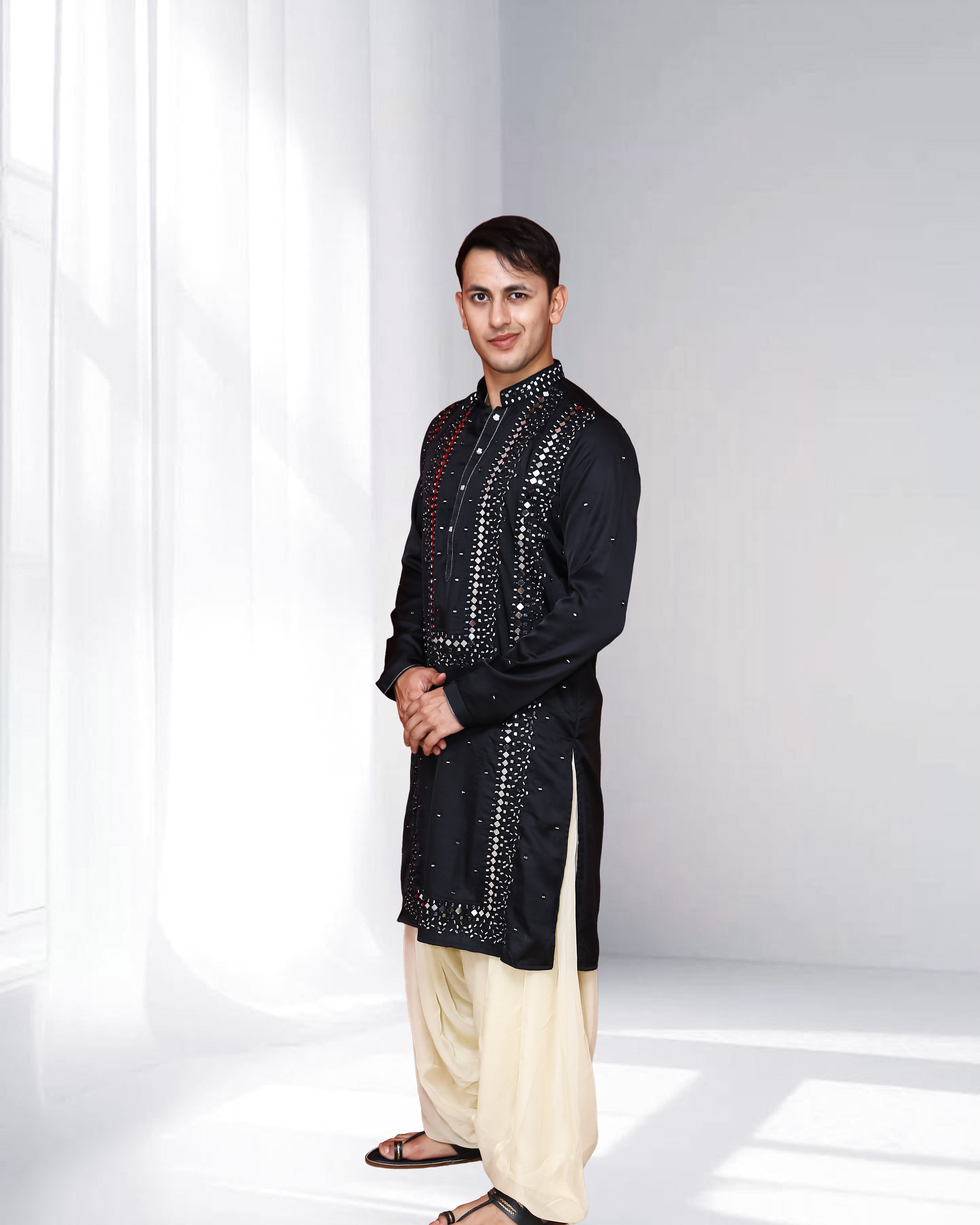 Man wearing a black sequined kurta with white pants on a white background