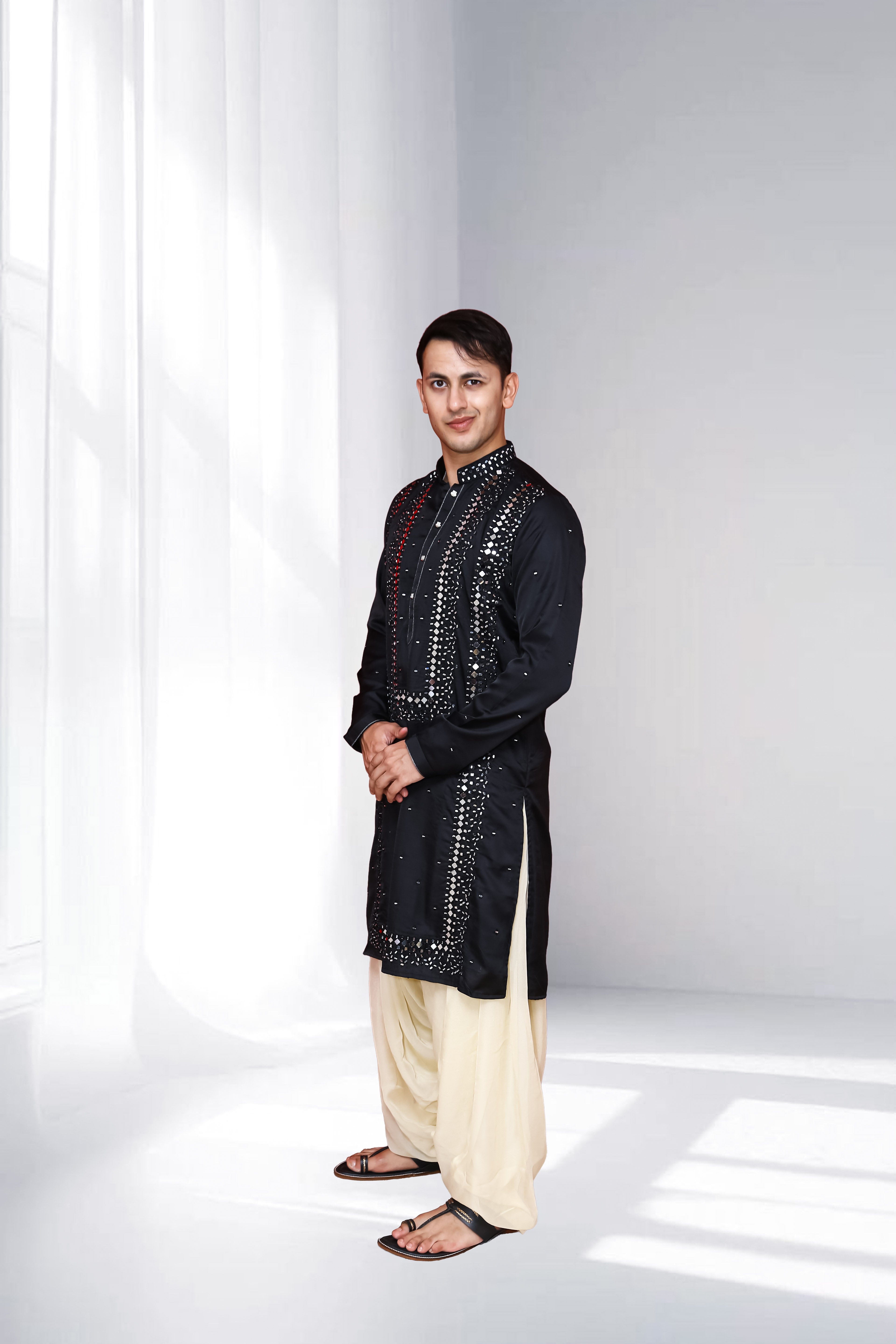 Man wearing a black sequined kurta with white pants on a white background