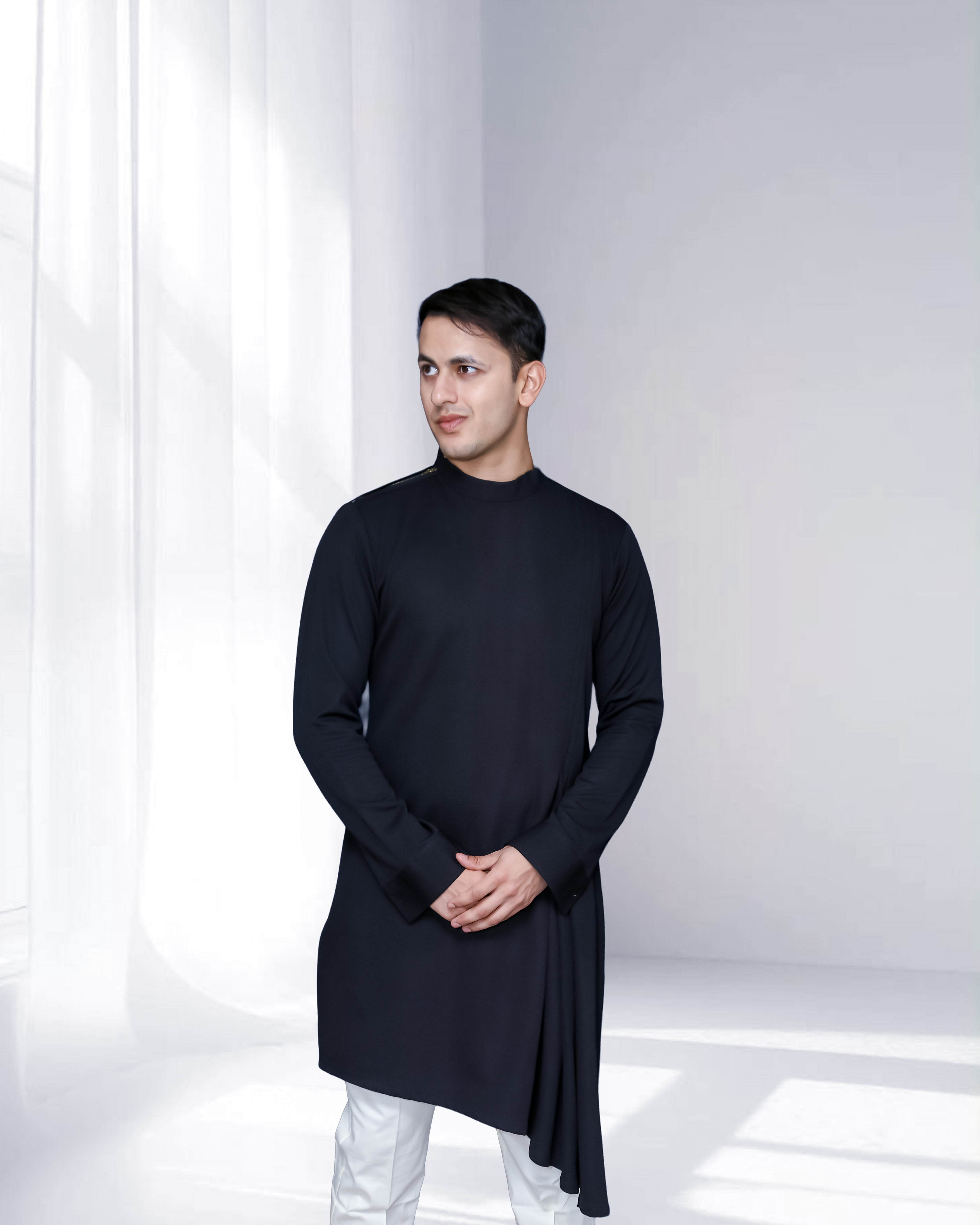 Man wearing a black long-sleeve shirt and white pants in a minimalistic setting