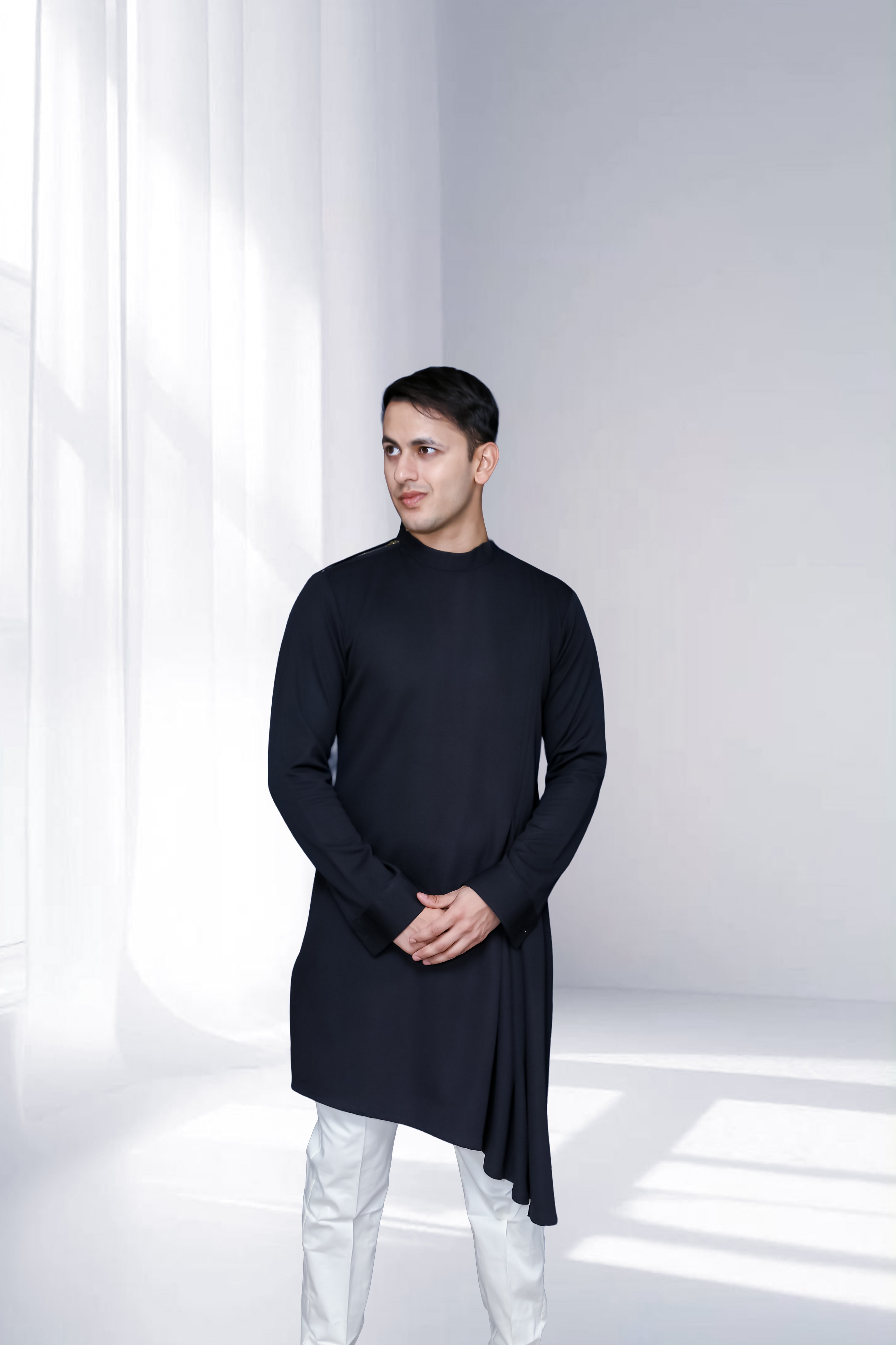 Man wearing a black long-sleeve shirt and white pants in a minimalistic setting