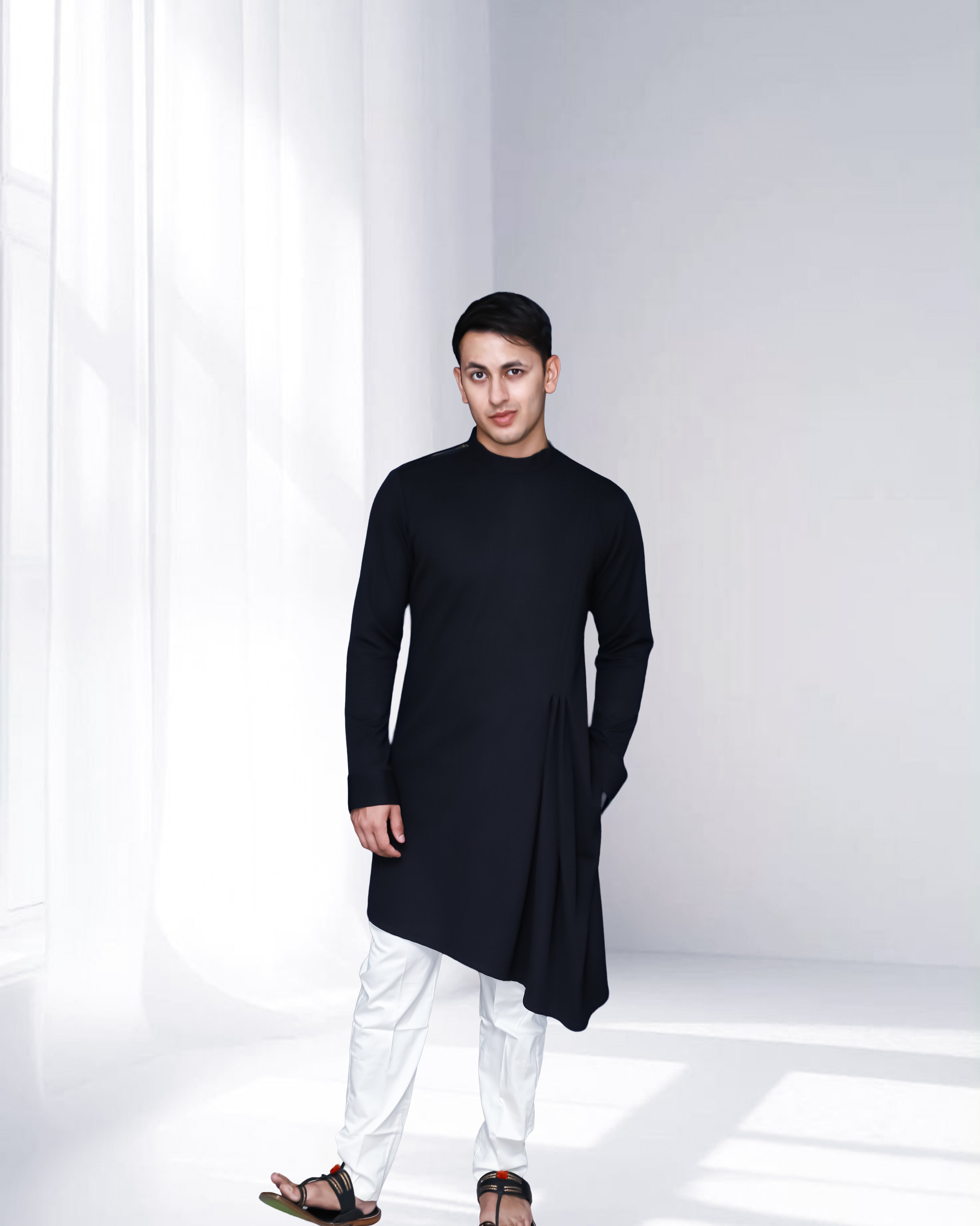 Person wearing a black kurta with white pants in a minimalistic setting