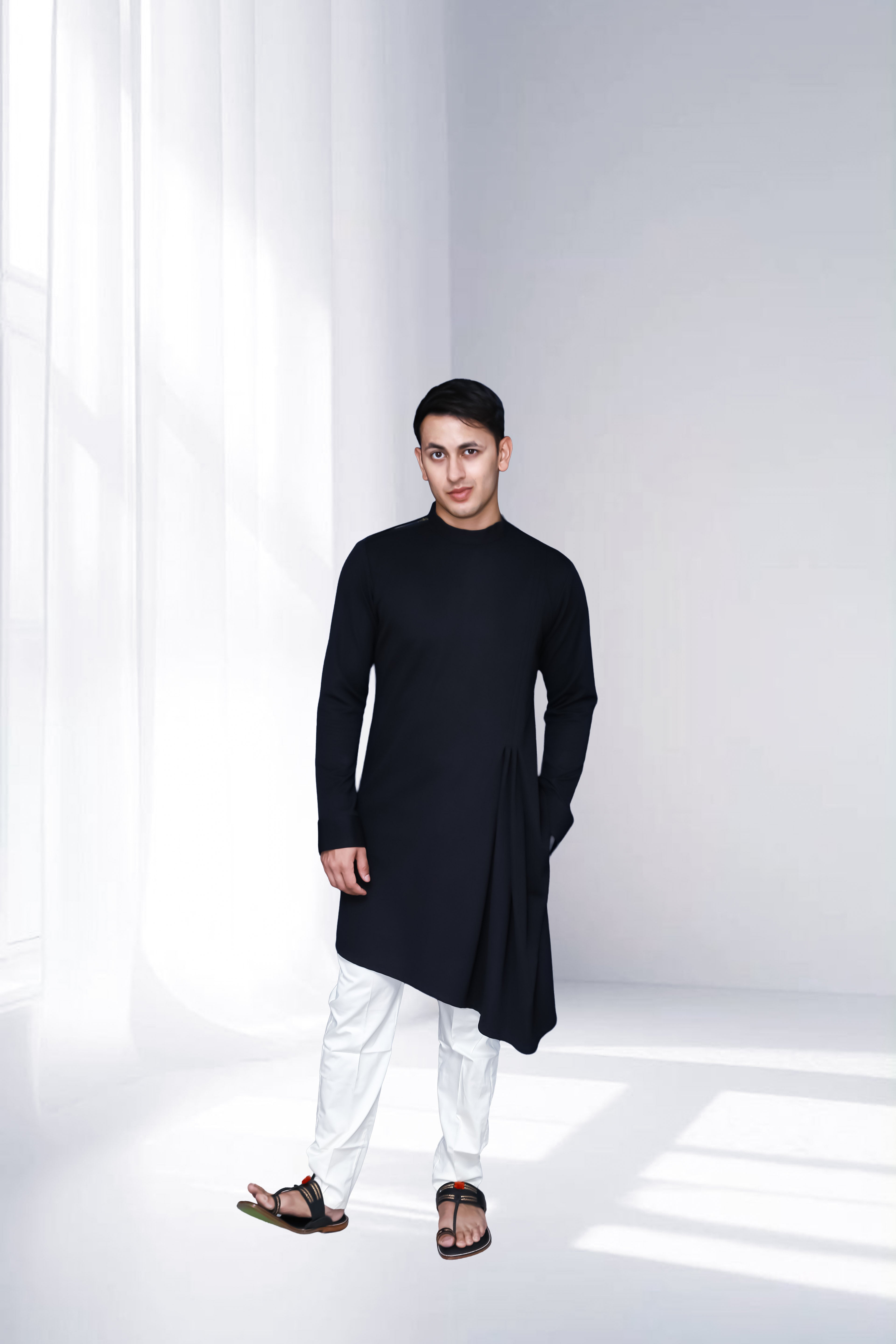 Person wearing a black kurta with white pants in a minimalistic setting