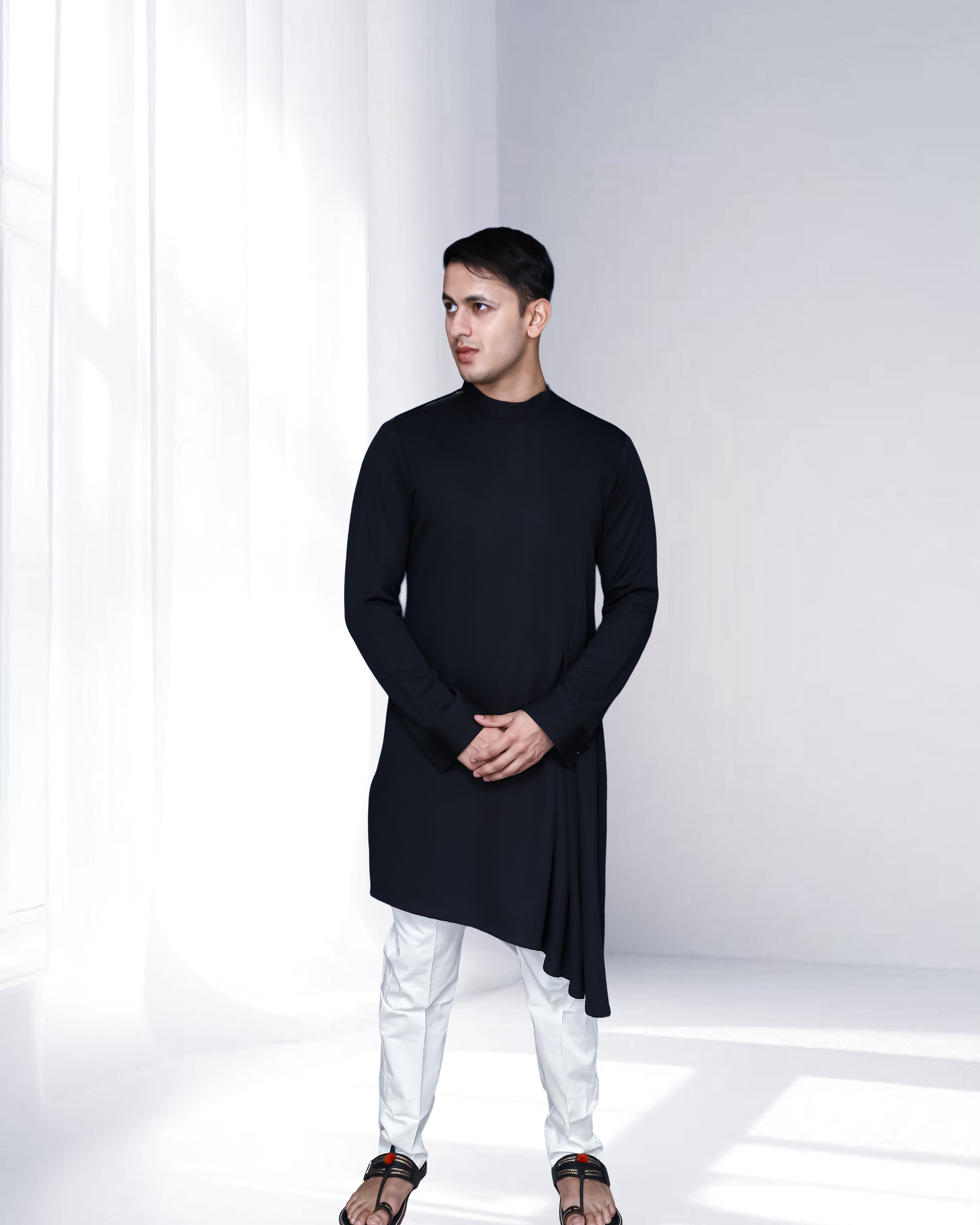 Man wearing a black kurta with white pants in a minimalistic setting