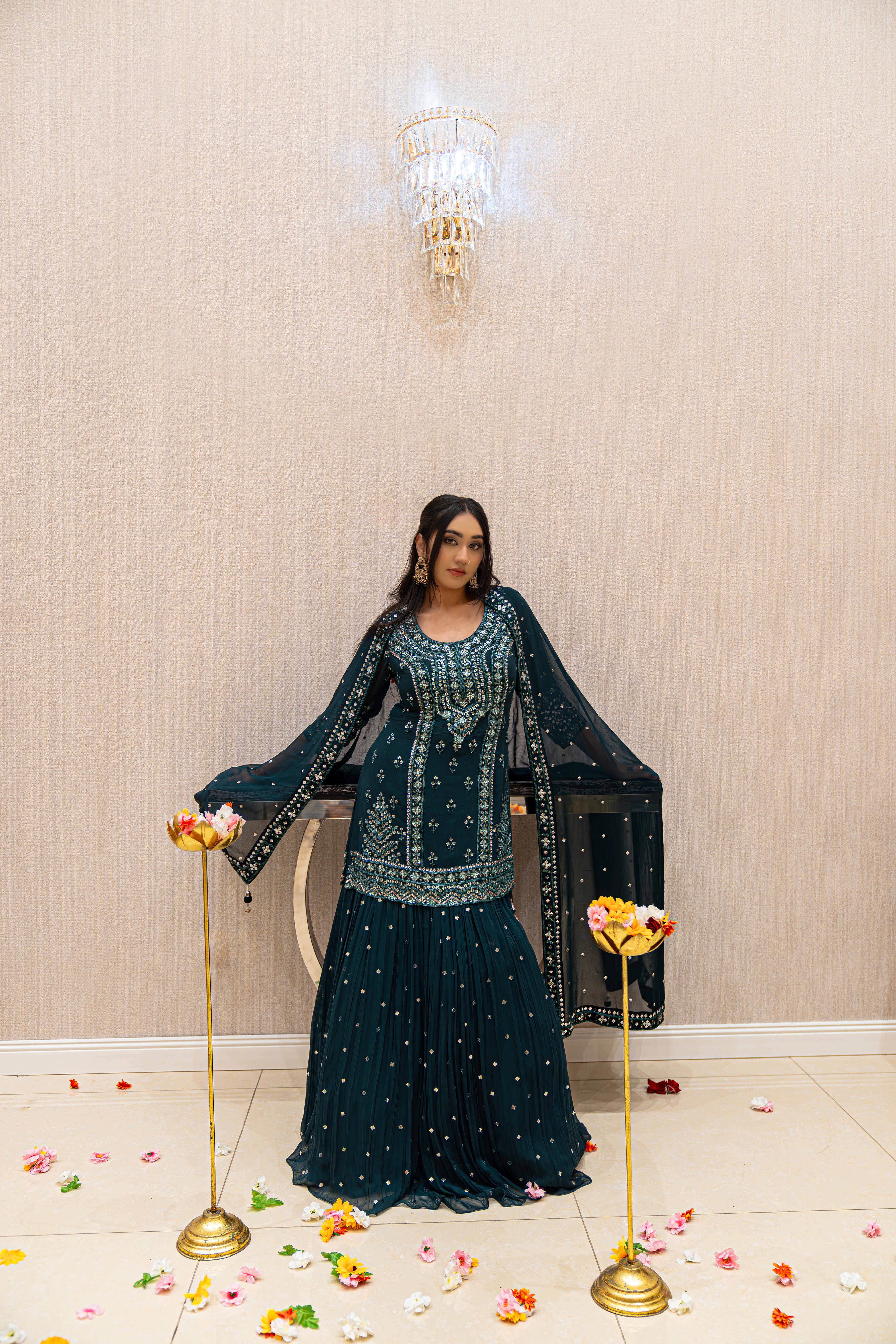 Woman in a dark green traditional outfit standing in a room with decorative elements.