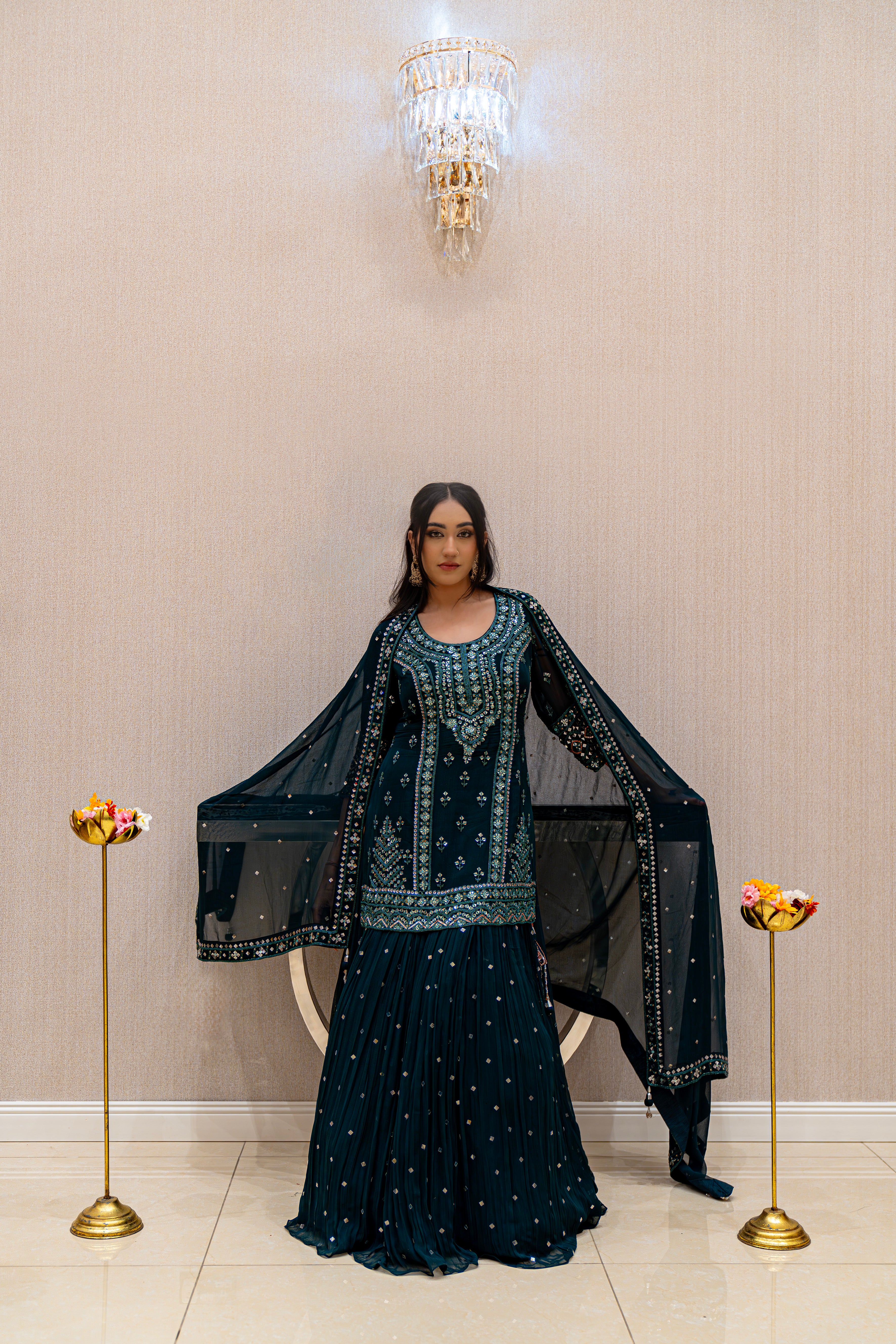 Woman in a dark green traditional outfit standing in a room with decorative elements.