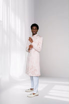 Man wearing a light pink kurta with white pants against a white background