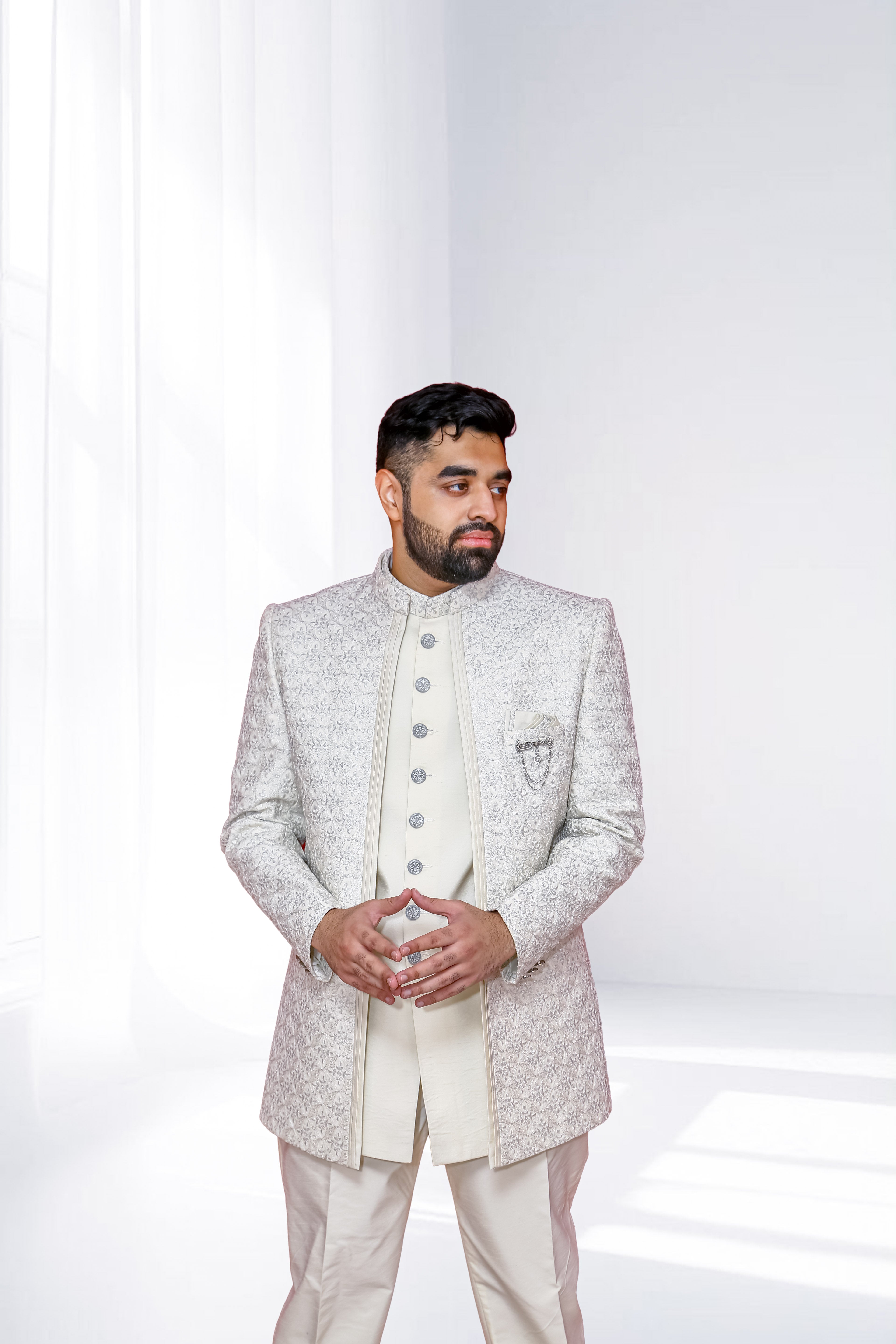 Man wearing a white embroidered Jodhpuri suit against a white background
