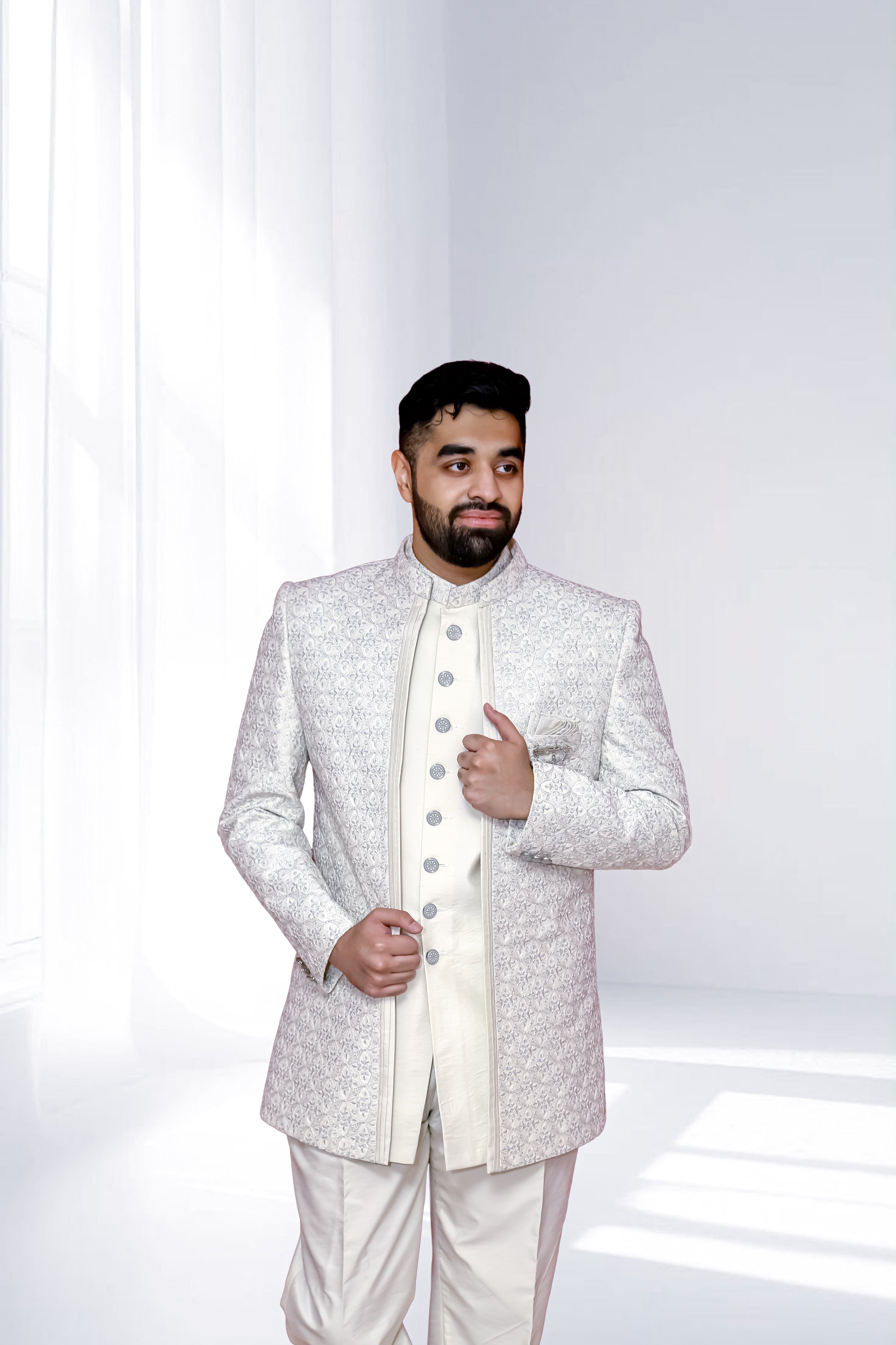 Man wearing a white embroidered Jodhpuri suit against a white background