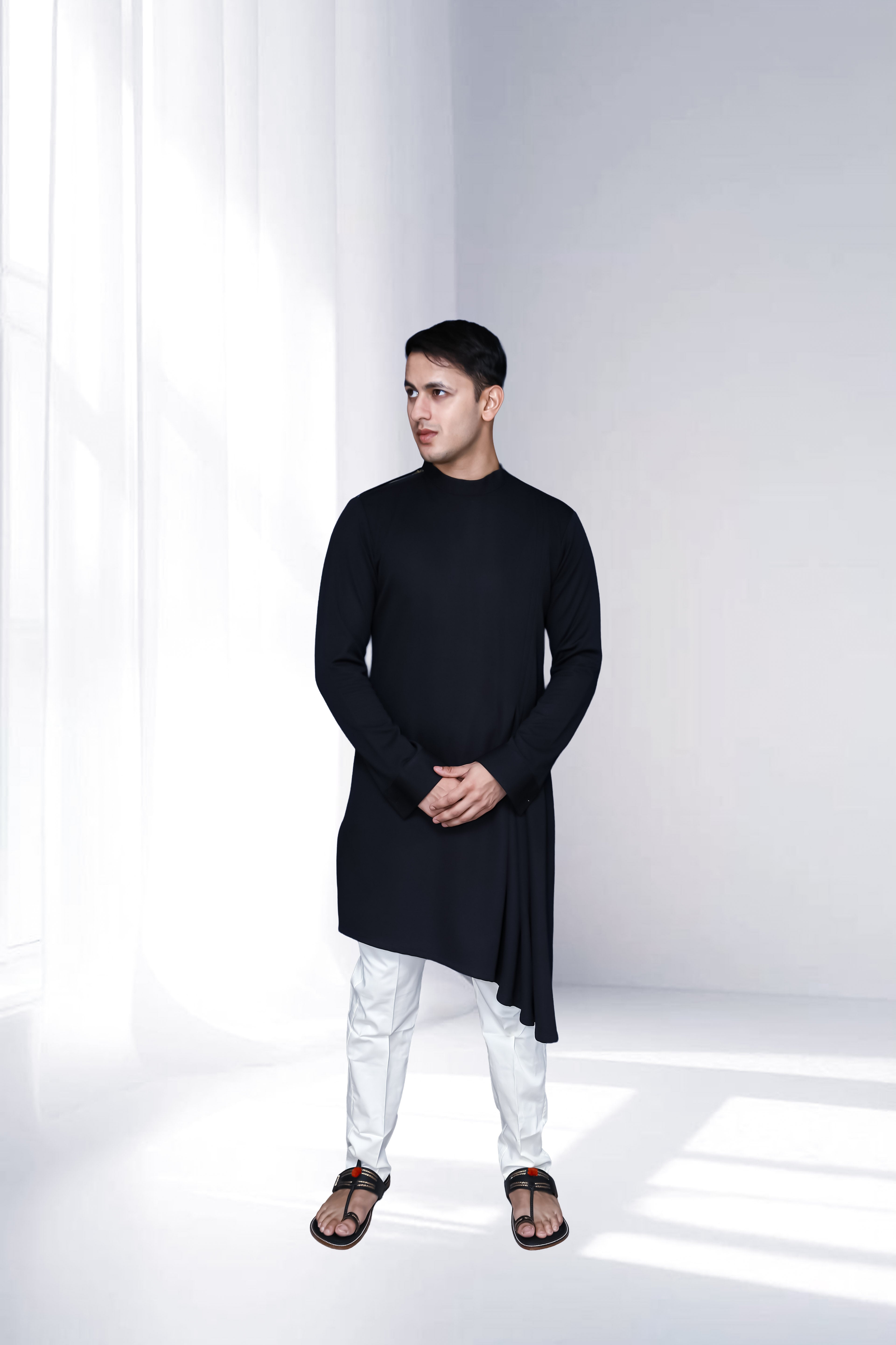 Man wearing a black kurta with white pants in a minimalistic setting