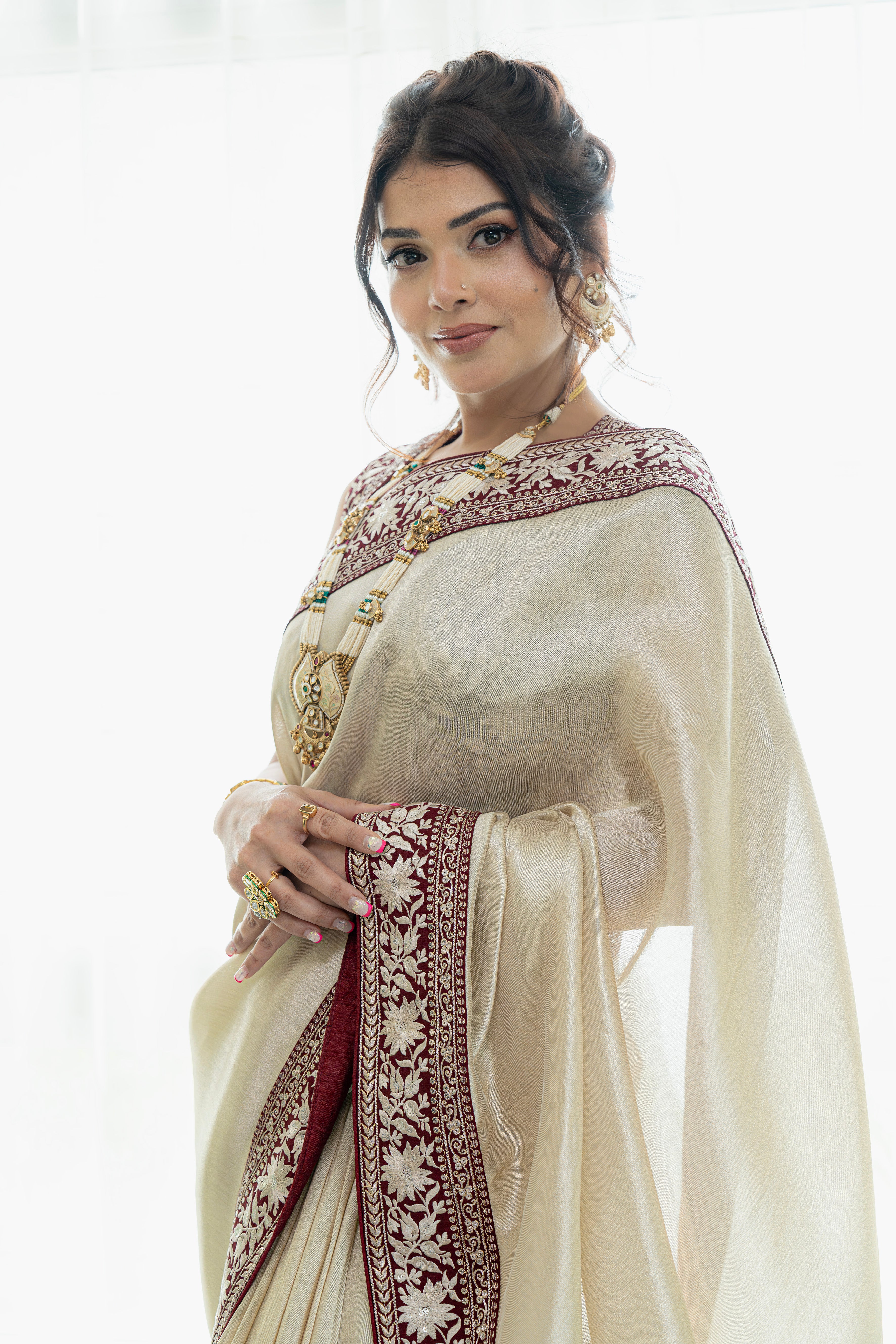 Woman wearing a traditional beige saree with intricate patterns on a white background