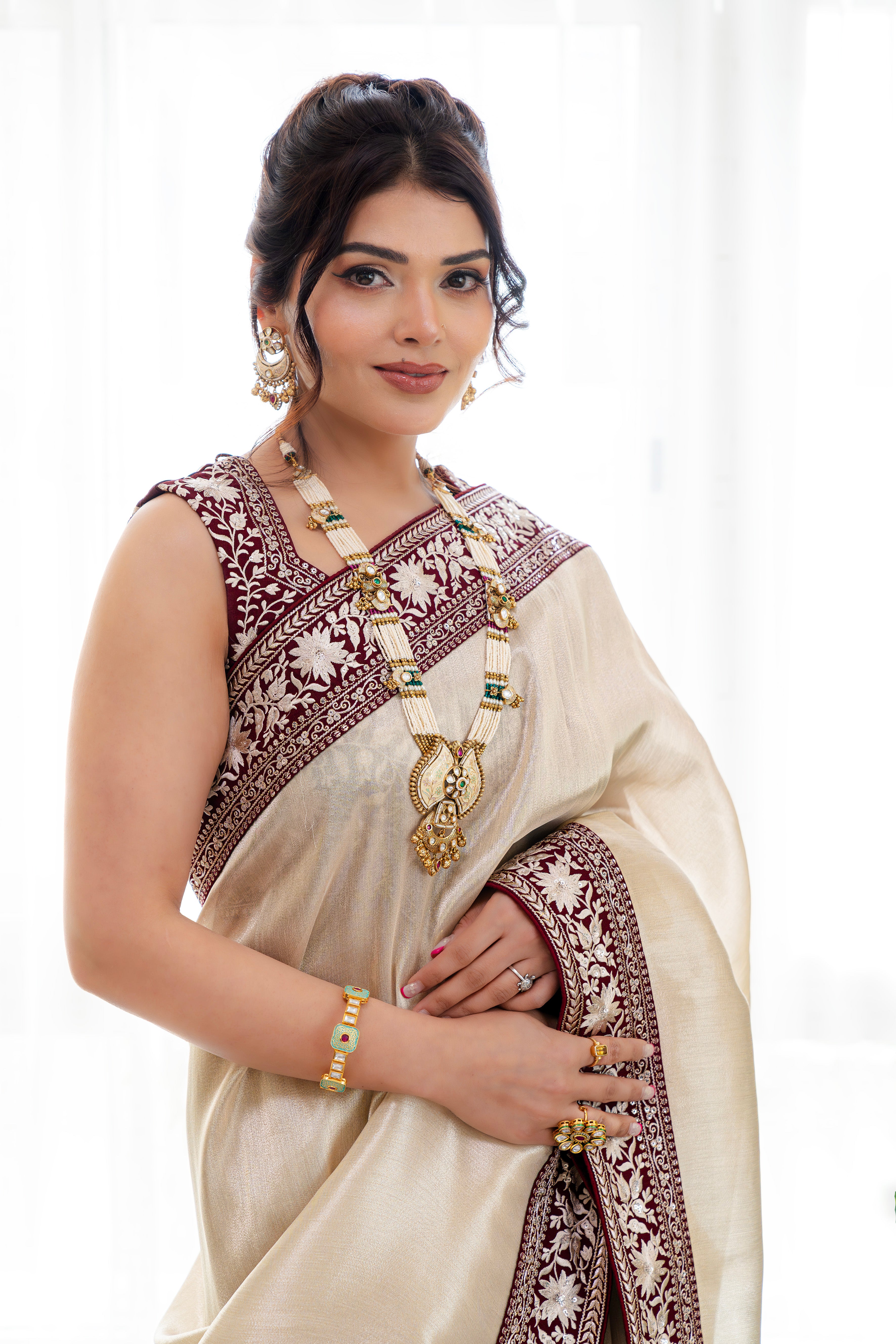 Woman wearing an elegant cream saree with a maroon embroidered border, styled indoors, perfect for weddings and festive occasions.