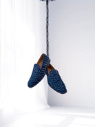 Pair of blue loafers with zigzag pattern hanging from a chain on a white background