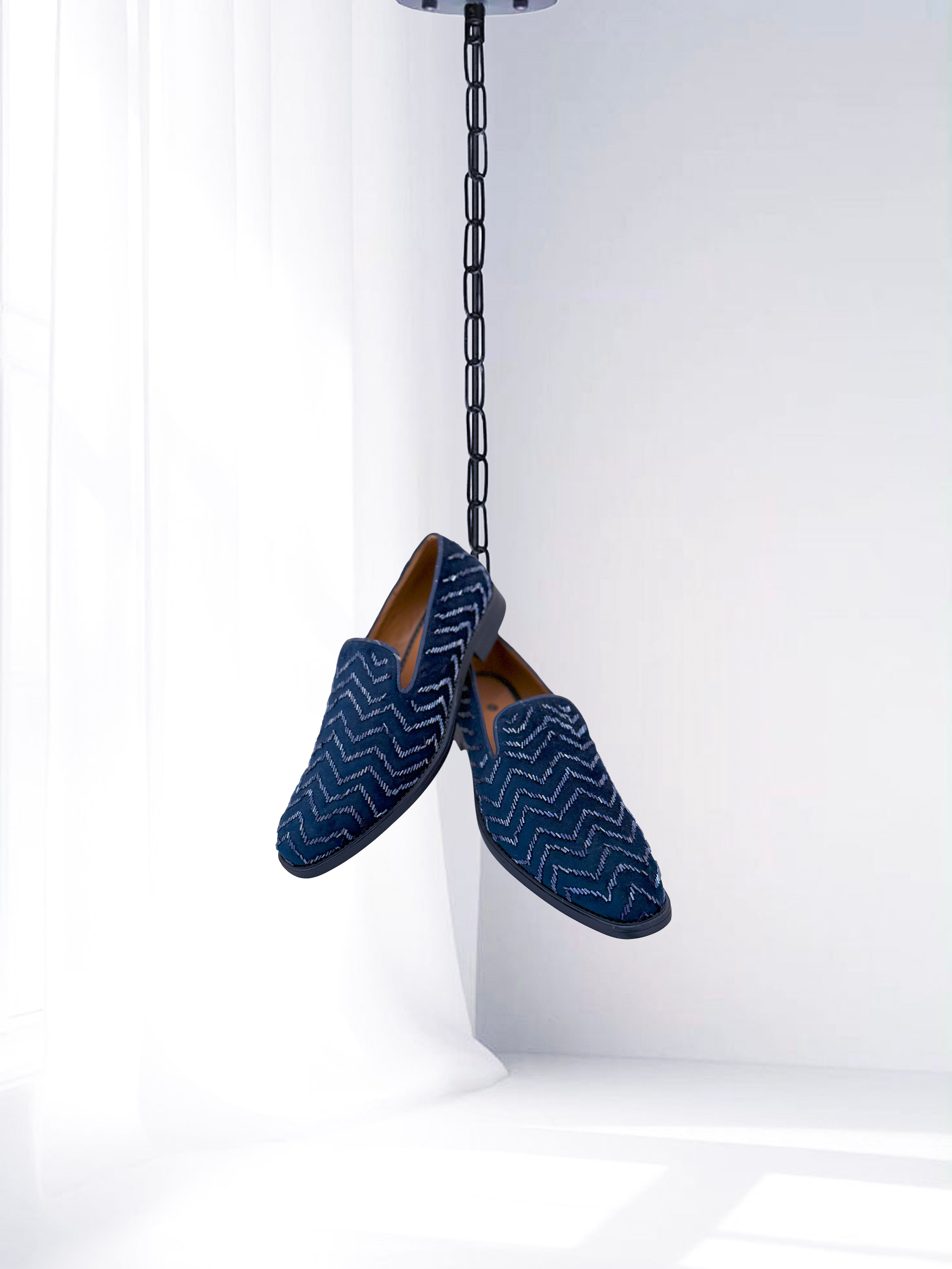 Pair of blue loafers with zigzag pattern hanging from a chain on a white background