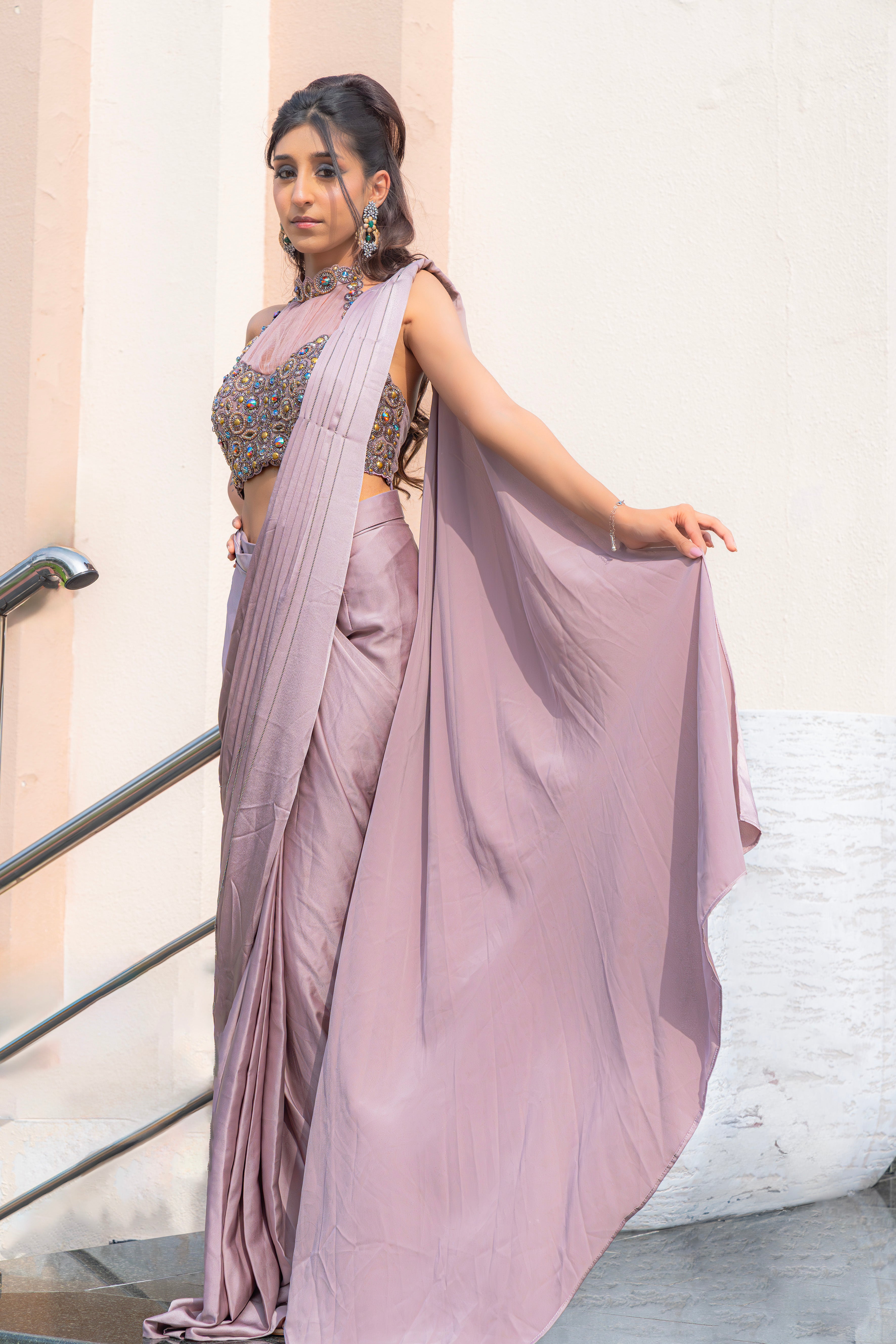Woman wearing an onion purple ready-to-wear saree styled with a jewelled halter neck pleated blouse, perfect for festive and formal occasions.