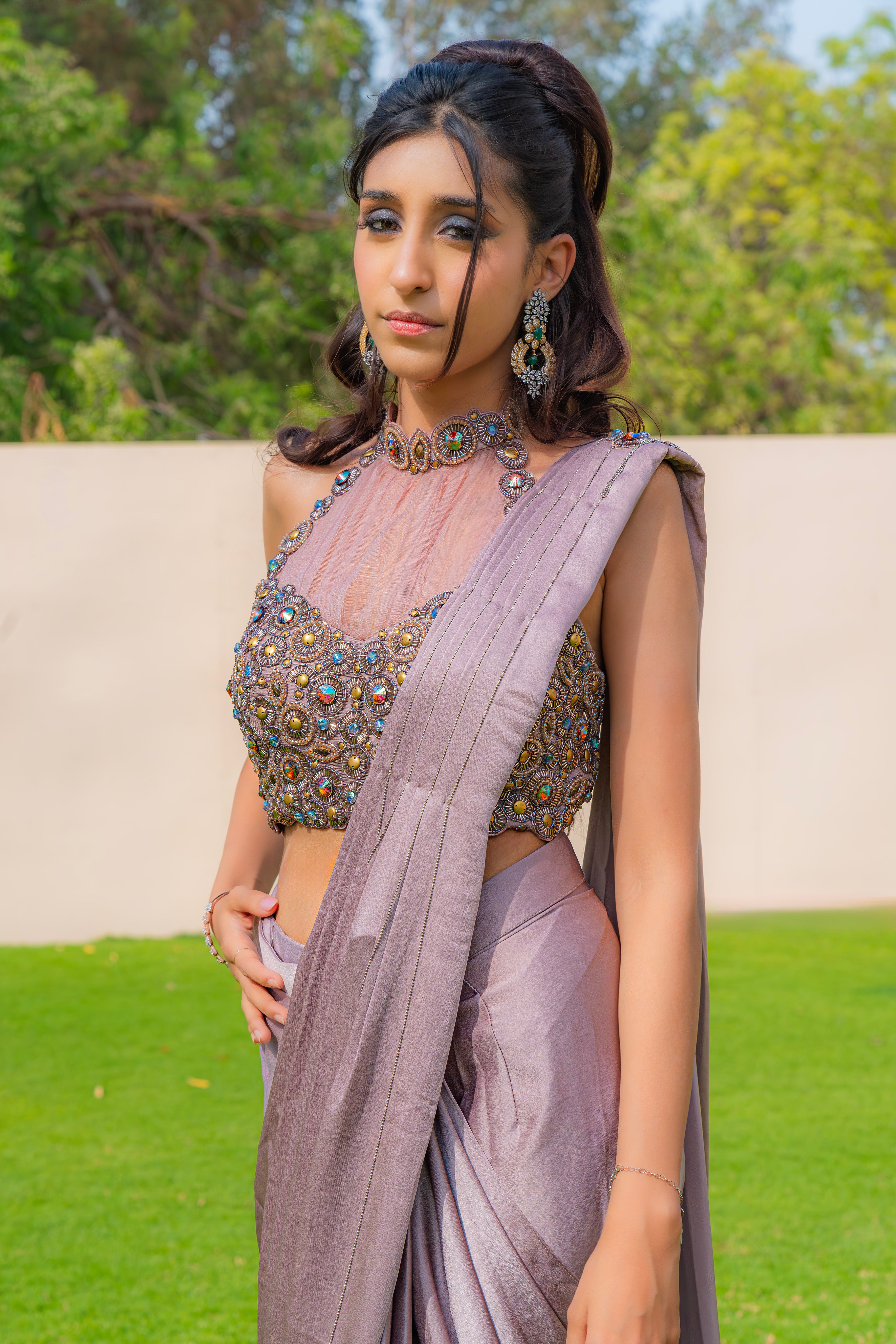 Woman wearing an onion purple ready-to-wear saree styled with a jewelled halter neck pleated blouse, perfect for festive and formal occasions.