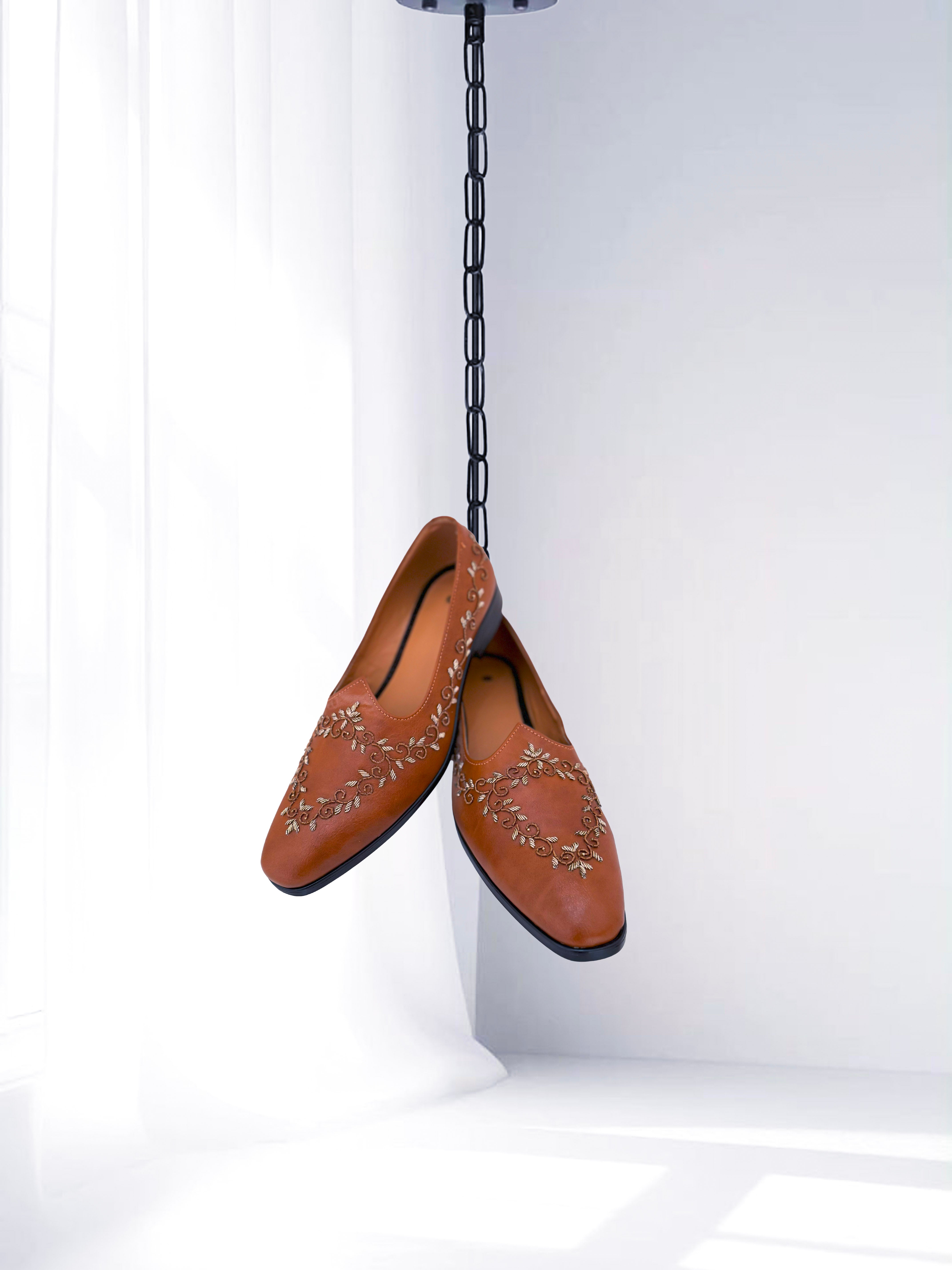 Tan leather loafers with intricate floral embroidery, traditional ethnic men’s shoes displayed against a white background